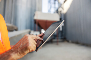 Senior male industry worker using tablet outdoors at industrial facility in safety vest