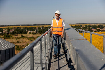 Senior Male Industry Worker Wearing Orange Safety Vest Outdoors On Facility Walkway