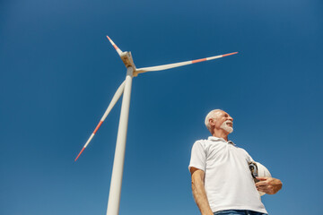 Senior environmentalist inspecting a large windmill at a solar farm on a bright clear sunny day