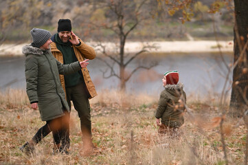 A mother, father, and son take a nature walk in a national park, warmly dressed, in the fall or winter without snow. Warm clothing for a hike for the whole family. Types of winter recreation