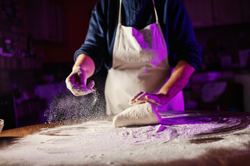 Baker kneading dough, sprinkling flour on table