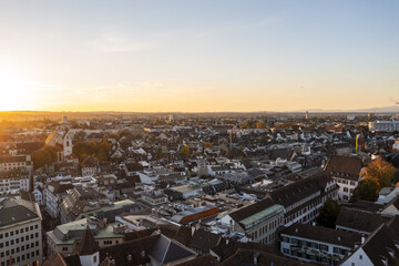 Aerial view of the city basking in the warm glow of the setting sun, casting long shadows over the rooftops and spires, Basel, Basel City, Switzerland.