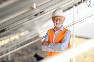 Senior male environmentalist wearing safety gear inspecting solar panels at solar farm