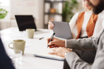 Team members discuss and write down ideas during a meeting in a bright office. They use laptops and tablets to share information and collaborate effectively.