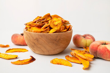 Dried peach slices in wooden bowl and fresh peaches on light background. Organic tasty sweet dried fruit, healthy dessert, vitamins and fiber. Food background, snack vegan flat lay top view