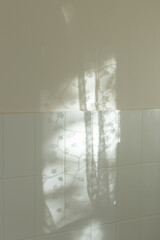 Minimal interior detail with soft natural sunlight casting delicate curtain shadows onto white ceramic tiles and light painted wall