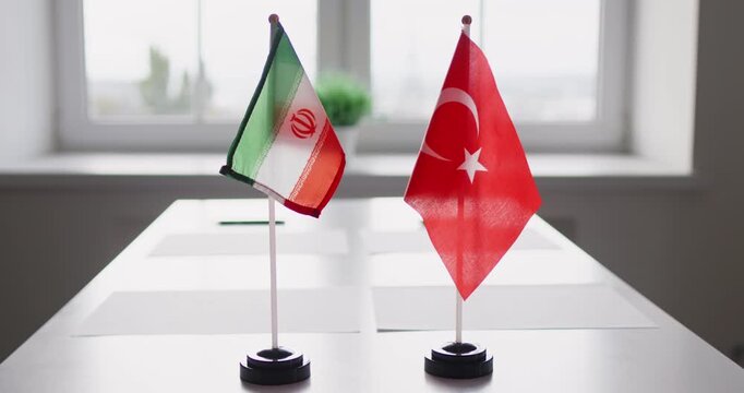 Diplomacy flags signal negotiation during bilateral meeting. Iran and Turkey mini table flags on stands suggest formal talks, agreement and partnership. Core idea: diplomatic talks theme.