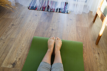 Top view of womans legs. Woman practicing yoga in living room on green sports mat