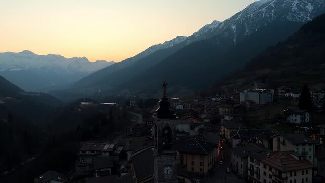 Aerial drone view over the church dome of Schilpario village in Val di Scalve, Italy, during a vibrant alpine sunset. drone above Presolana mountains, and the peaceful landscape of the Alpi Orobie