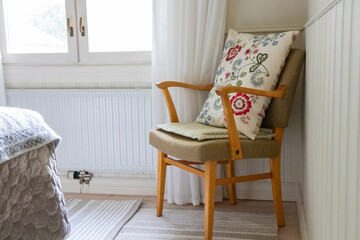 Mid-century modern Scandinavian armchair with wooden frame and curved design, featuring a floral embroidered cushion. Bright, cozy interior with light, airy Nordic style © alma.photo