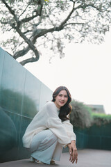 Young woman crouching outdoors smiling in casual sweater