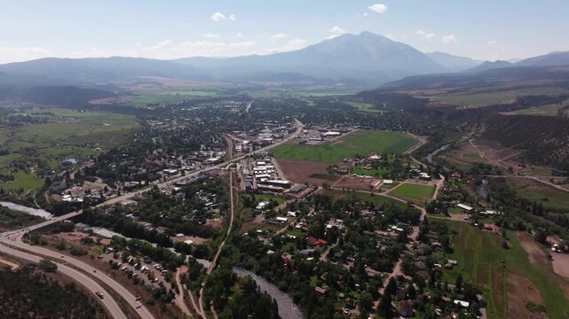 Expansive elevated overview of Carbondale neighborhoods with grid-like streets, tree-lined homes, and distant Mount Sopris partially hazed in atmospheric light