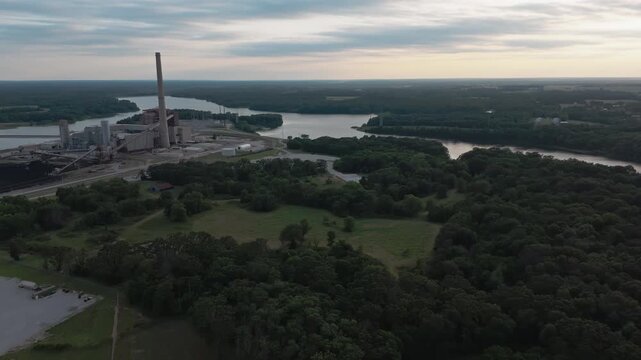 Drone orbit counter clockwise around coal power plant and cooling lake in forest at dusk