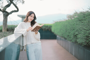 Young woman enjoying a book outdoors, reflecting on glass barrier