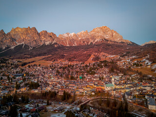 Aerial view of the town nestled in the valley, with the majestic Dolomites glowing in the warm light of dusk, Cortina d'Ampezzo, Veneto, Italy.