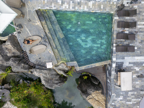 Aerial view of a woman lies down on a sun bed next to an emerald pool, nestled amidst rocky terrain and stone pathways, offering a tranquil escape, H&Atilde;&nbsp; Giang, H&Atilde;&nbsp; Giang, Vietnam.