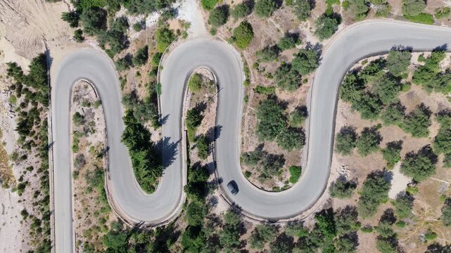 Aerial view of a winding road cutting through the landscape, with a lone car navigating its curves, Himare, Vlore County, Albania.