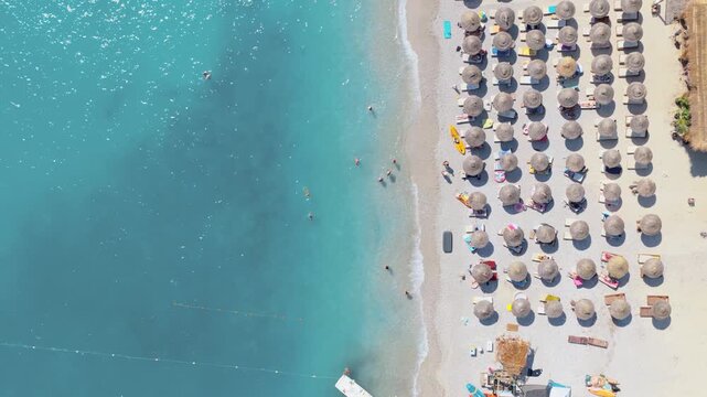 Aerial view of pristine turquoise waters meeting a sandy beach dotted with neatly arranged umbrellas, creating a striking contrast, Himare, Vlore County, Albania.
