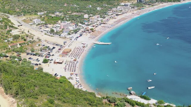 Aerial view of the vibrant Himare beach with its golden sands contrasting with the clear turquoise waters and boats, Himare, Vlore County, Albania.