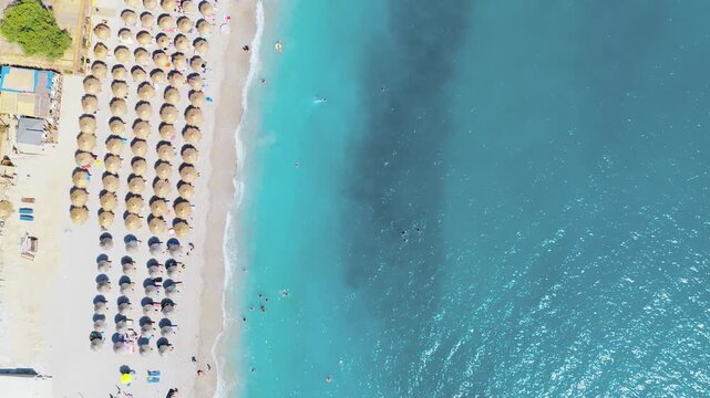 Aerial view of beach umbrellas dotting the sandy shoreline next to the turquoise waters, Himare, Vlore County, Albania.