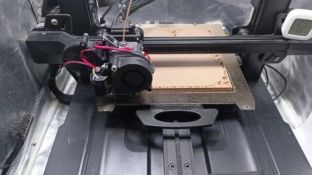 Detailed close-up shot of a Fused Deposition Modeling (FDM) 3D printer nozzle extruding light brown filament, building a complex container layer by layer.