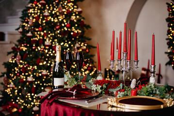 Christmas banquet table with candles, served with dishes, glasses and a bottle of champagne stands...
