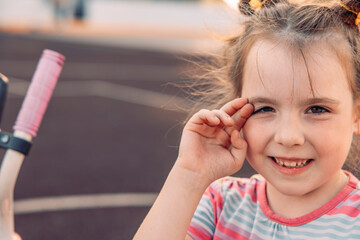 A young girl with brown hair and playful pigtails smiles while standing on a court. She wears a striped shirt and enjoys quality time outdoors.