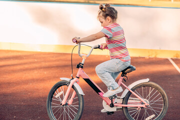 Caucasian girl rides a pink bicycle on sunny day. She in protective gear, smiles, enjoying quality time outdoors
