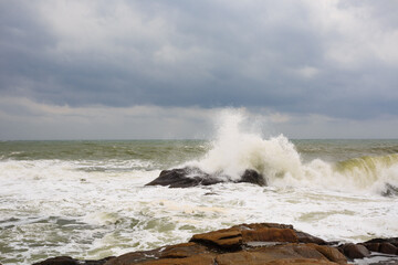Under a cloudy sky, the waves crashed against the massive rocks, creating huge surges. (Scenic view of Hainan Stone Park, China)