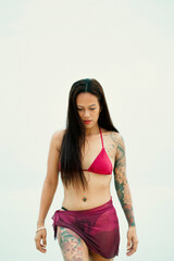 Woman with tattoos walking into calm tropical sea, red bikini and minimalist beach aesthetic