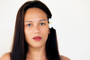 Studio portrait of woman with white flower in hair, bare shoulders and calm gaze on white background