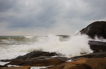 Under a cloudy sky, the waves crashed against the massive rocks, creating huge surges. (Scenic view of Hainan Stone Park, China)