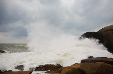 Under a cloudy sky, the waves crashed against the massive rocks, creating huge surges. (Scenic view of Hainan Stone Park, China)