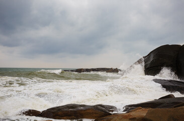 Under a cloudy sky, the waves crashed against the massive rocks, creating huge surges. (Scenic view of Hainan Stone Park, China)