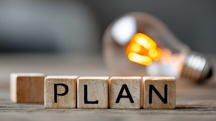 Wooden blocks spell the word plan with a glowing light bulb in background emphasizing strategy and ideas for business development and success.
