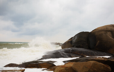 Under a cloudy sky, the waves crashed against the massive rocks, creating huge surges. (Scenic view of Hainan Stone Park, China)