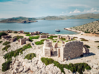 Aerial view of ancient stone ruins meet the turquoise sea, framed by rugged, sun-kissed islands under a vast sky, Kornati, Sibensko-kninska zupanija, Croatia.