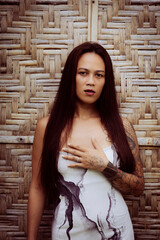 Confident woman in long printed dress standing in front of bamboo wall, intense expression and tropical editorial style