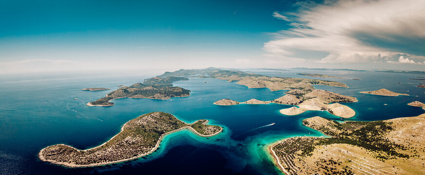 Aerial view of the islands in the Adriatic Sea sparkle with turquoise waters meeting the rugged, sun-kissed shores under a vast, bright sky, Kornati, Sibensko-kninska zupanija, Croatia.