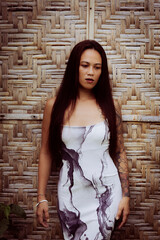 Tattooed woman wearing printed dress in front of bamboo backdrop, strong body language and identity portrait