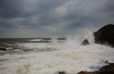 Under a cloudy sky, the waves crashed against the massive rocks, creating huge surges. (Scenic view of Hainan Stone Park, China)