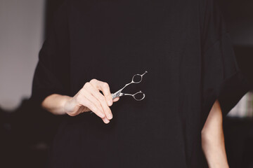 Barber or Hairdresser holds precision shears in hand on dark background. Professional in beauty industry