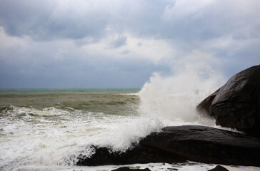 Under a cloudy sky, the waves crashed against the massive rocks, creating huge surges. (Scenic view of Hainan Stone Park, China)