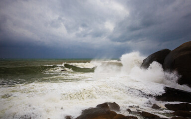 Under a cloudy sky, the waves crashed against the massive rocks, creating huge surges. (Scenic view of Hainan Stone Park, China)