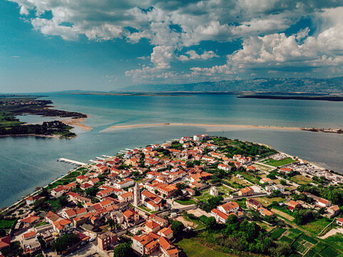 Aerial view of the old town's red rooftops contrast against the azure sea and Nin lagoon, a tranquil scene under a sky dotted with clouds, Nin, Zadar County, Croatia.