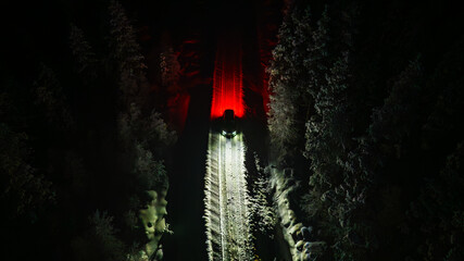 Aerial view of a snow-covered train piercing through the darkness, its red lights blazing against the wintry forest, Salla, Lapland, Finland.