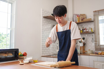 Young man sprinkling flour on raw dough, preparing fresh homemade pastries in a modern kitchen. Embracing a hobby