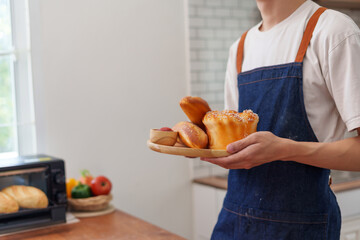 Man in an apron presenting a wooden tray with homemade sweet pastries and bread, fresh from the oven, for breakfast