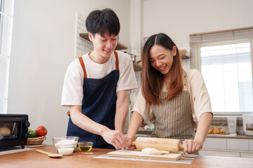 Young Asian couple collaborating in the kitchen, rolling dough for homemade bread. Sharing joyful moments while cooking at home