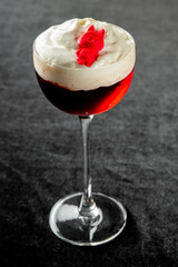 A close-up vertical shot of a layered red and white cocktail/dessert in an elegant stemmed glass, garnished with a small red gummy bear